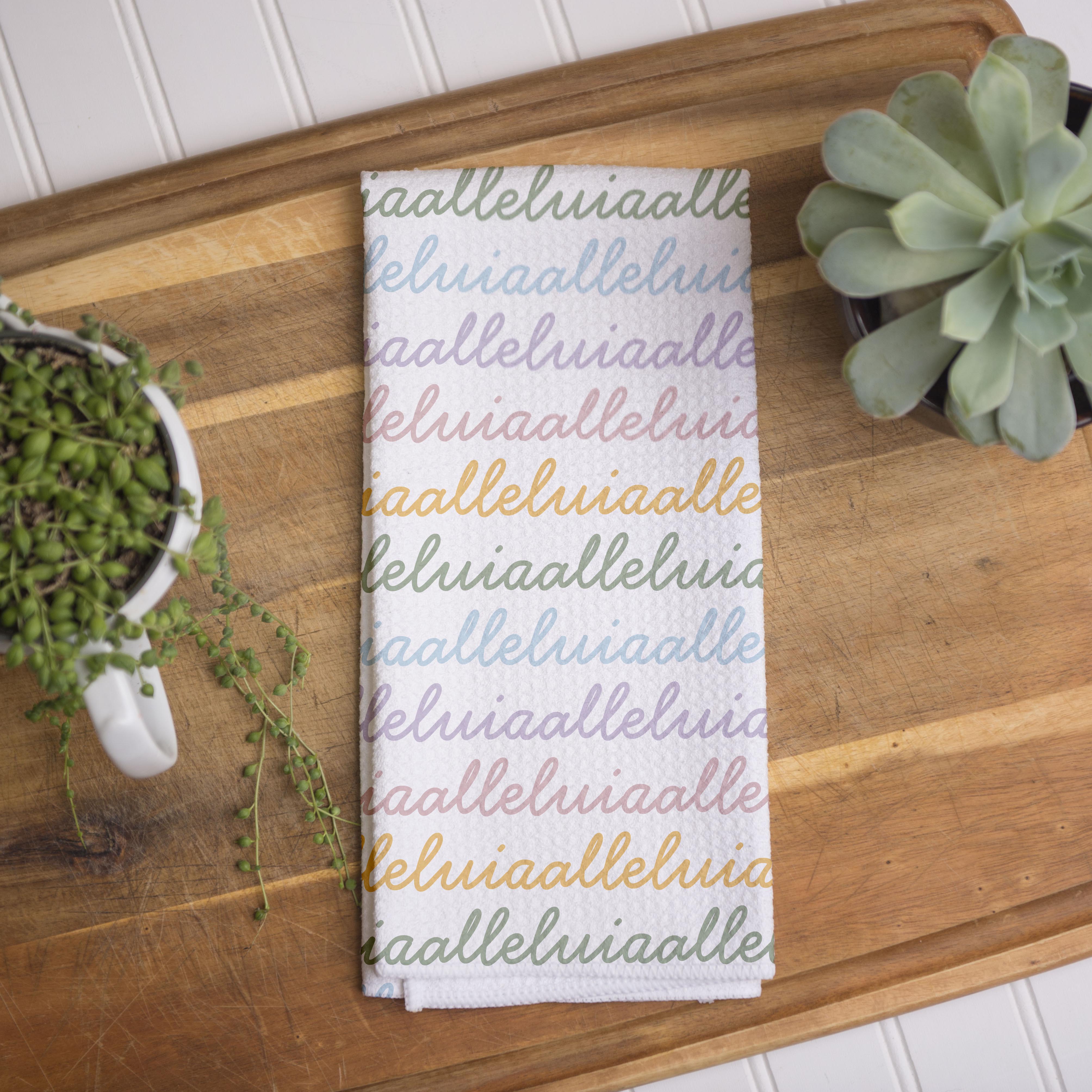 White colored, waffle textured dish towel folded in half with the design that says alleluia, alleluia repeatedly in cursive writing, in colors pastel pink, pastel yellow, pastel blue and pastel green.