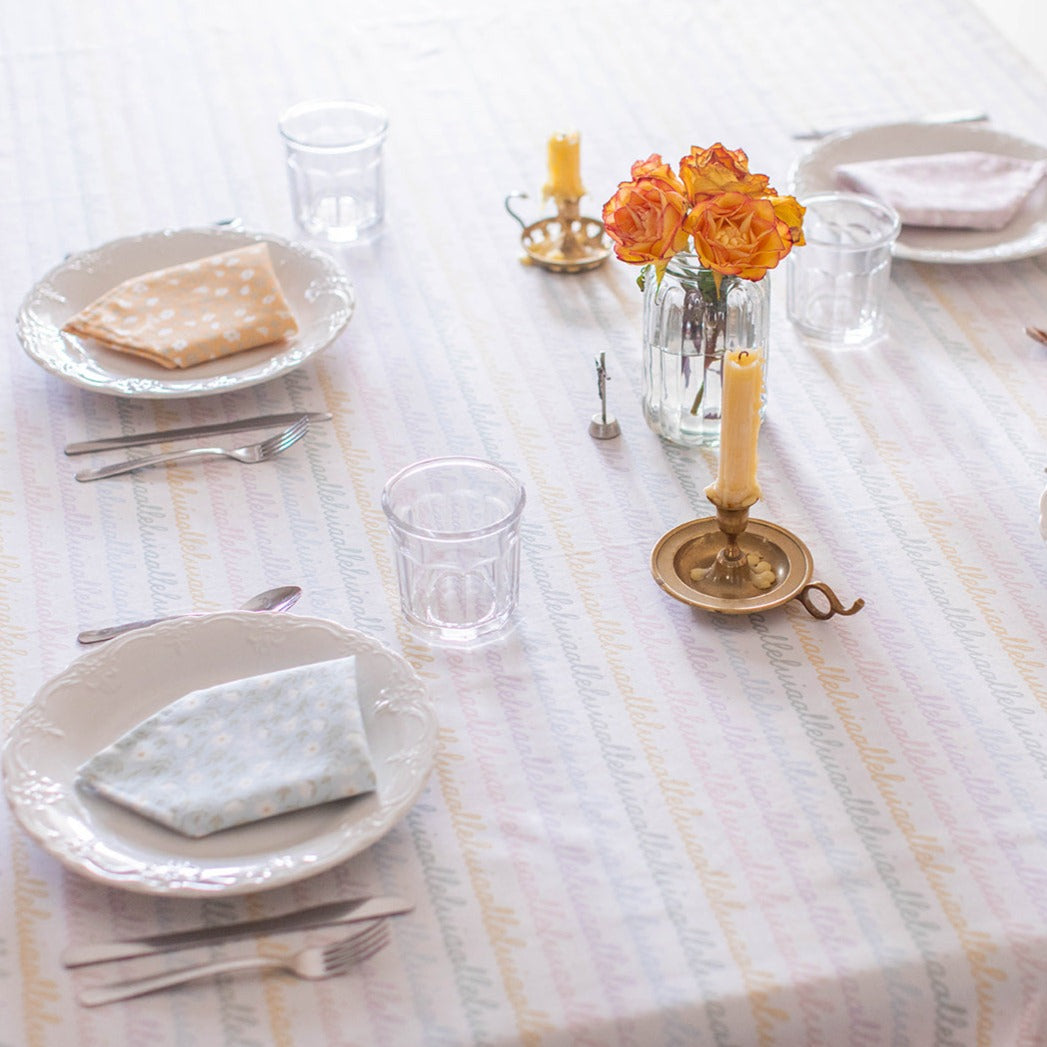 Three colored Easter Alleluia napkins with white floral design, neatly placed on a plate set on a table.