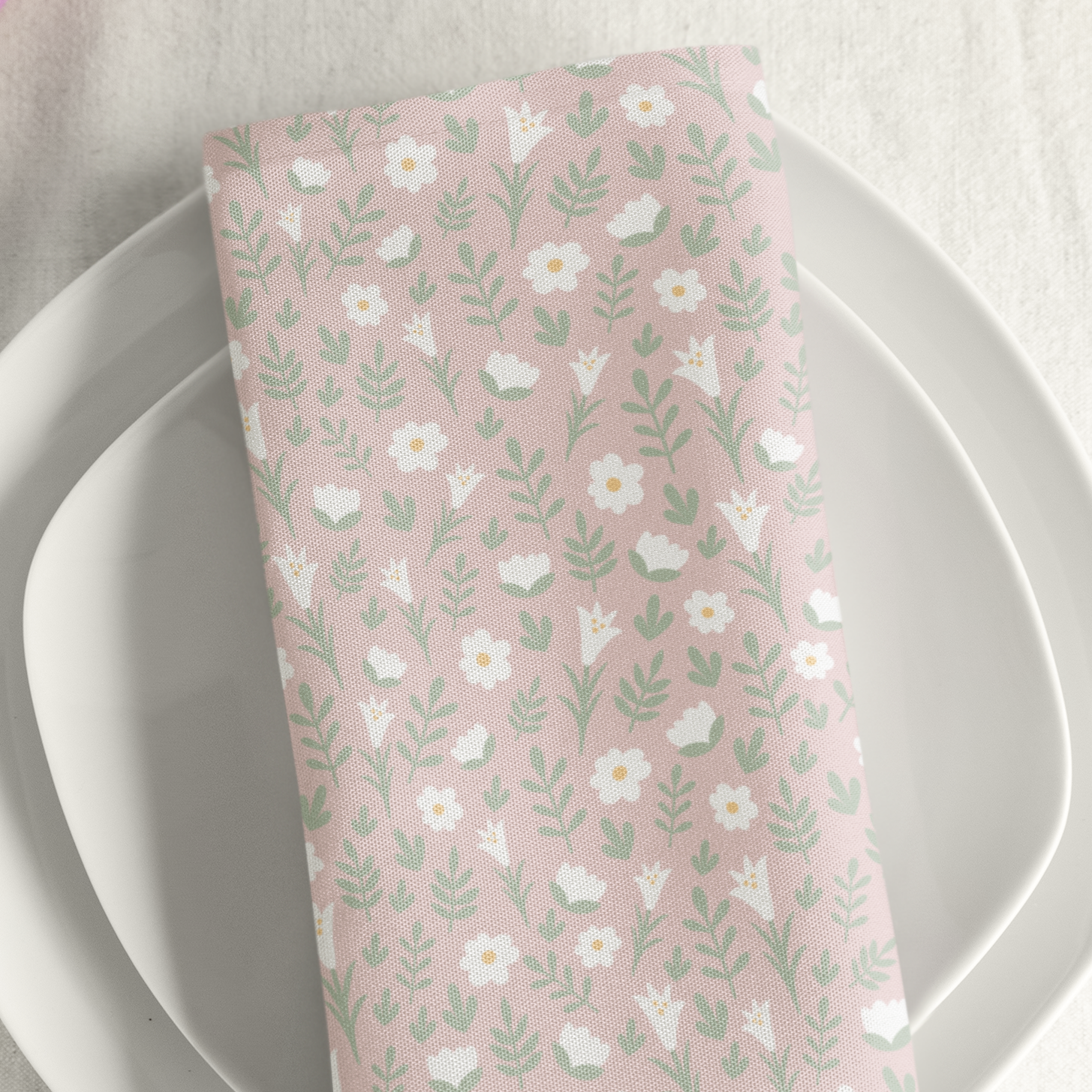 Light pink Easter Alleluia napkin with white floral design placed on a plate in a styled table setting.
