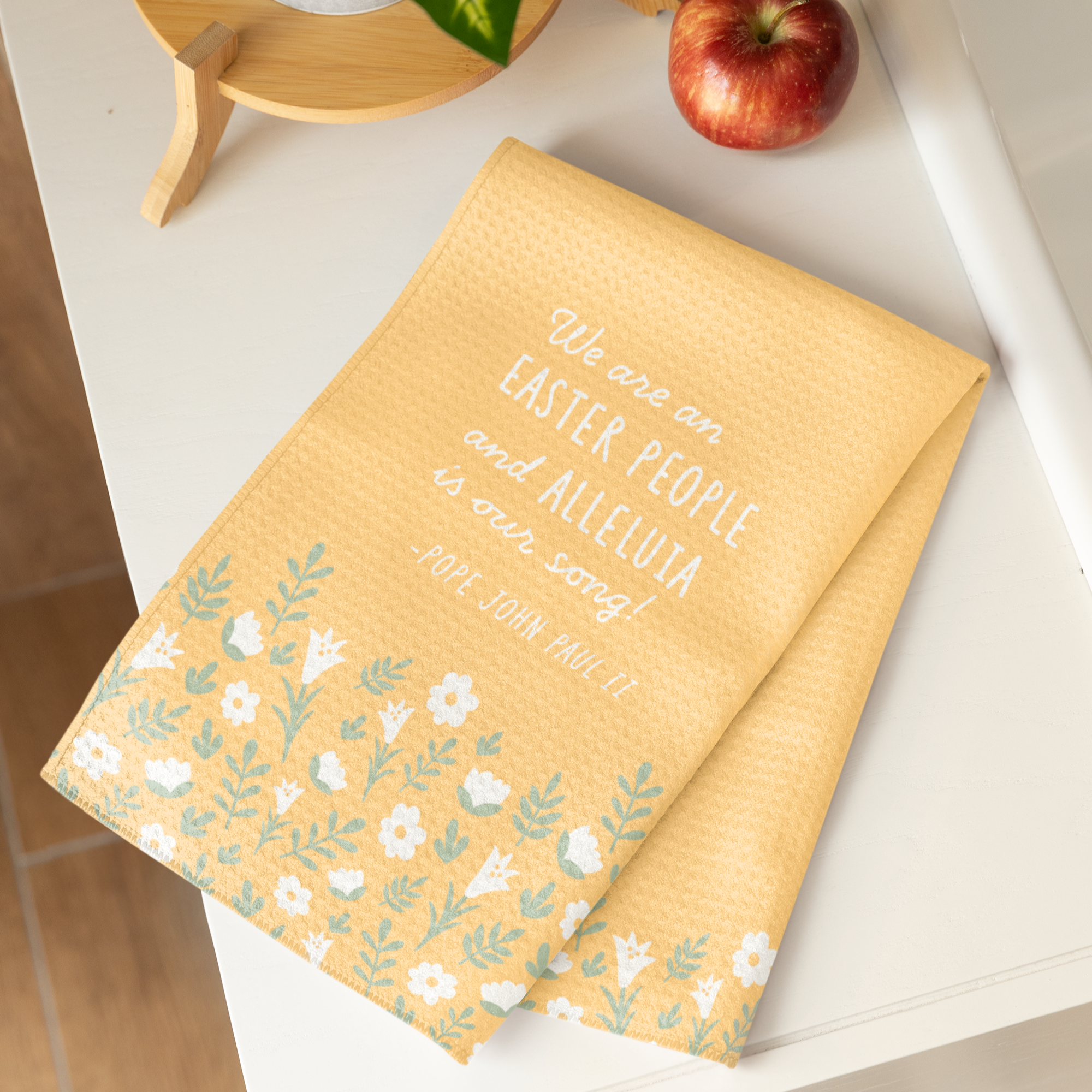 Yellow, waffle textured dish towel, folded in half, showing the design of subtle white flowers and pale green leaves with the wordings that say "We are an EASTER PEOPLE and ALLELUIA is our song! -Pope John Paul II"