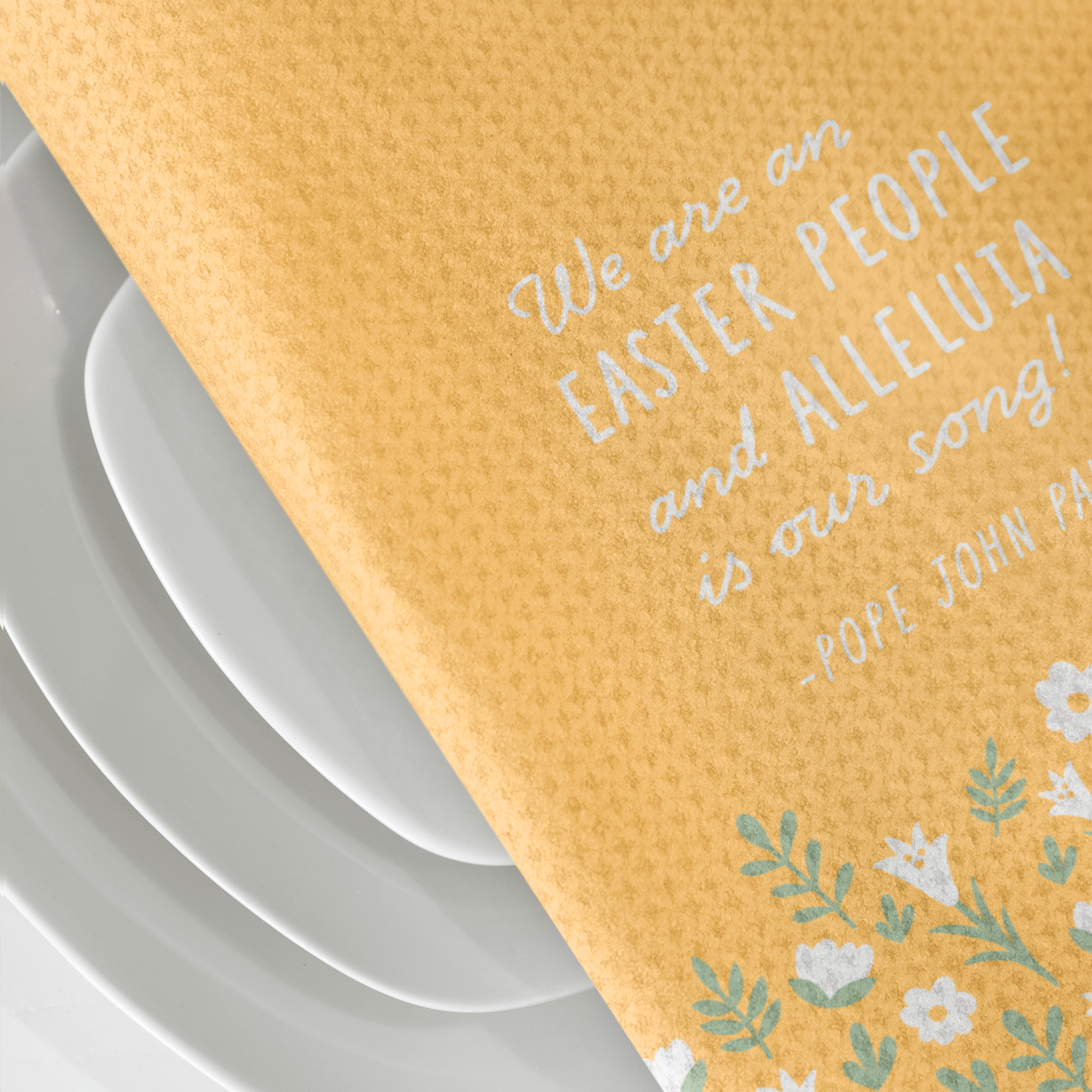 Yellow, waffle textured dish towel, folded in half, showing the design of subtle white flowers and pale green leaves with the wordings that say "We are an EASTER PEOPLE and ALLELUIA is our song! -Pope John Paul II"
