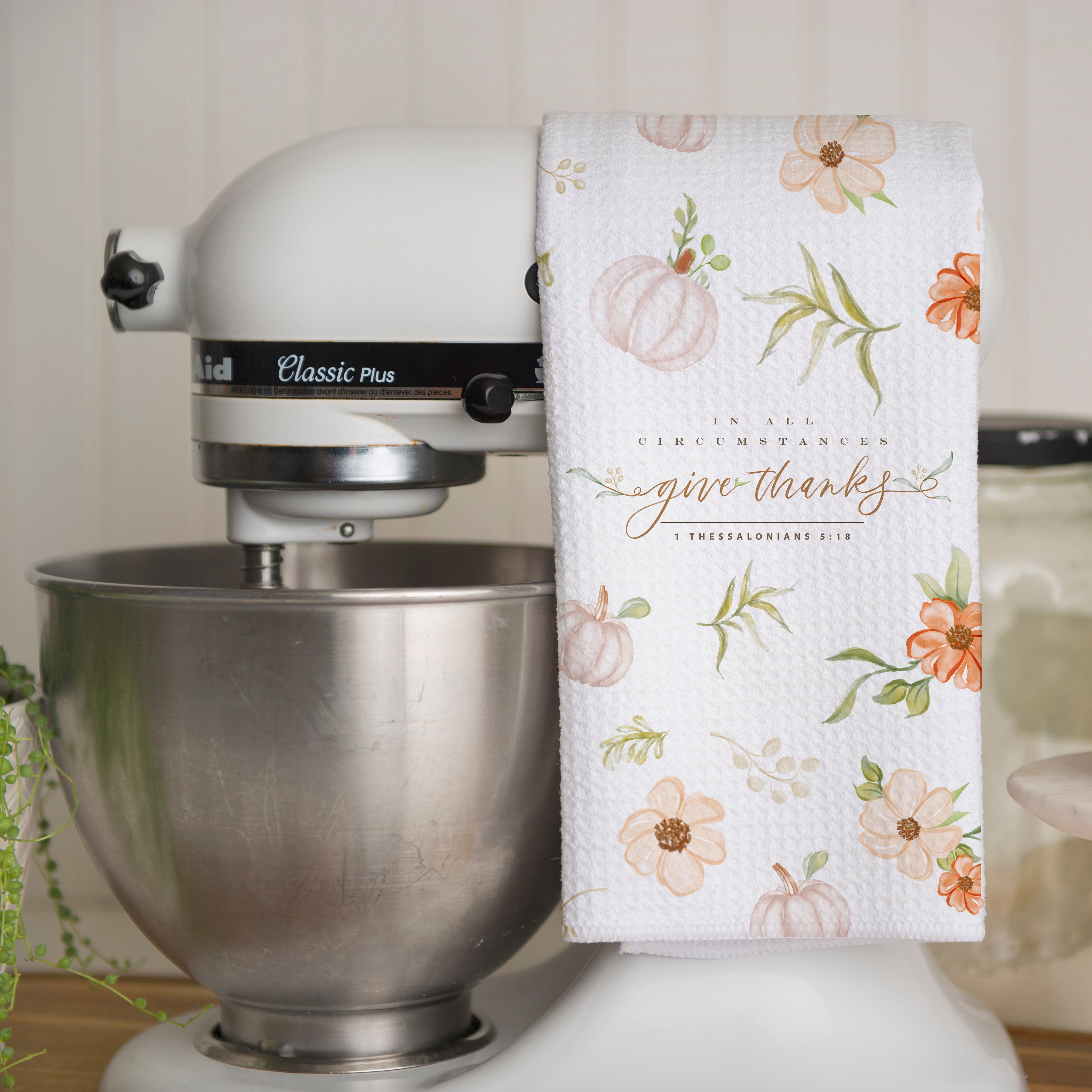Kitchen mixer with a floral towel draped over it, next to a small plant on a white surface.